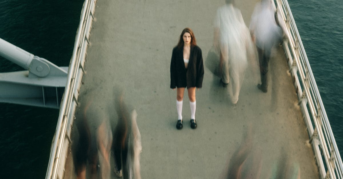 A woman stands still on a bustling footbridge, capturing a moment of solitude amidst motion.