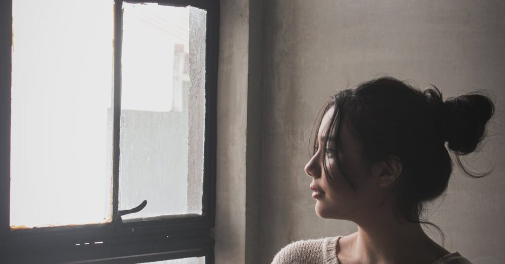 A woman in a cozy sweater looks thoughtfully out a window, creating a serene and contemplative mood.